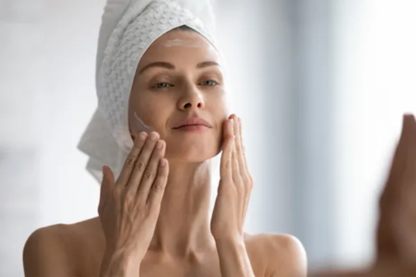 Kobieta w białym ręczniku na głowie nakłada krem na twarz